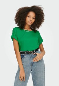 Grønn T-skjorte med korte ermer og rullekanter, brukt sammen med høytlivde lyseblå jeans og et svart belte med en rund spenne.