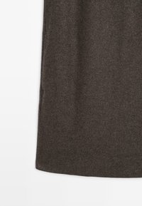 Sukně z tmavě hnědé tkaniny vzoru rybí kosti se rovnými lemy, která je vystavena na bílém pozadí, zdůrazňující texturu a detaily šití.