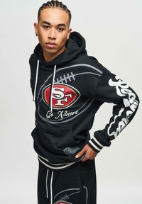 Felpa nera con cappuccio caratterizzata da lacci bianchi, grafiche grigie di football e un logo rosso e oro dei San Francisco 49ers. Include strisce laterali.