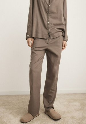 Brune løstsiddende bukser kombineret med matchende skjorte med knapper og beige slip-on sko på tæppebelagt gulv.