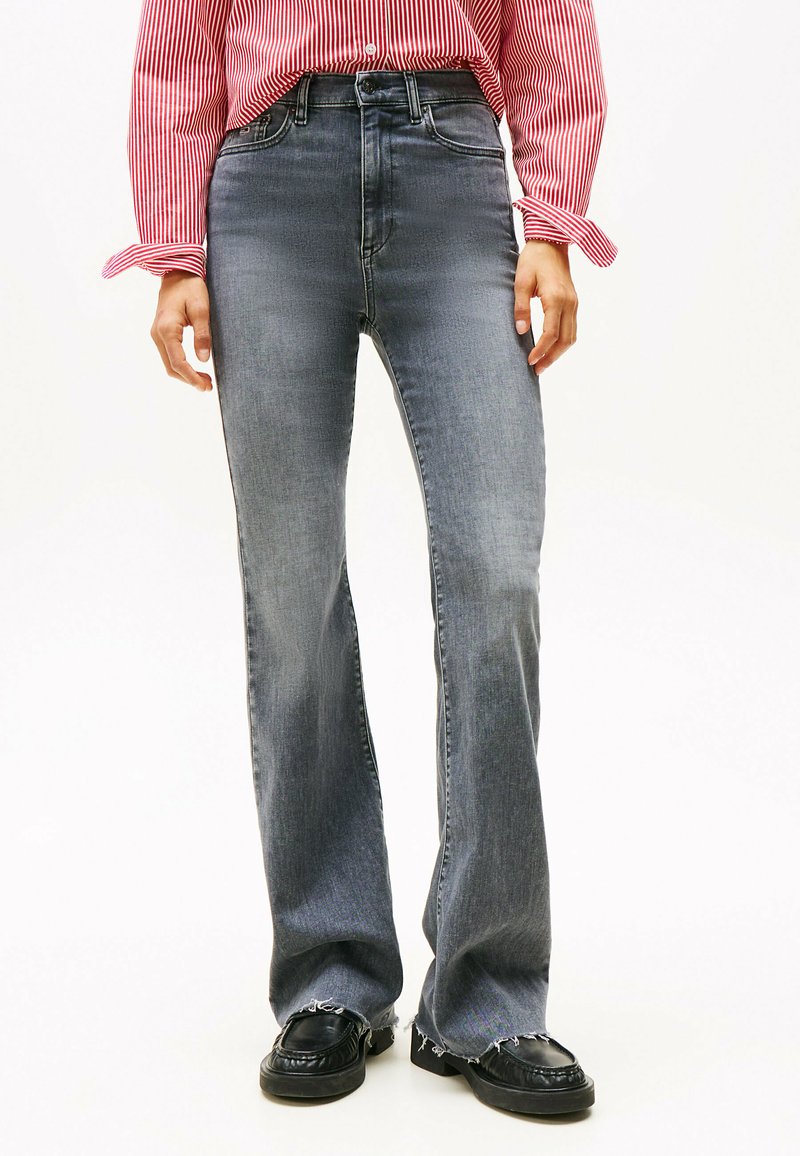 Højtaljede, udvidede grå denimjeans med en falmet finish, der har et fem-lomme-design og frynset kant, båret med sorte sko.