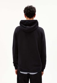 Sweat-shirt à capuche noir avec une coupe décontractée, doté d'un ourlet et de poignets côtelés. Le matériau semble doux, avec une texture lisse.