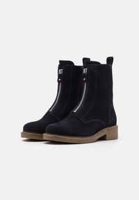 Botines de ante en azul marino oscuro con costuras contrastantes, cremalleras laterales y tacón plano. Diseño clásico adecuado para varios conjuntos.