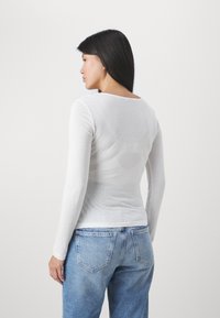 Camisa blanca de manga larga con cuello redondeado, hecha de una tela ligera, combinada con jeans de mezclilla de tiro alto color azul claro.
