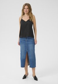 Camisole en satin noir à fines bretelles, assortie à une jupe en denim longueur genoux avec une fente sur le devant, en délavé moyen bleu. Escarpins noirs à enfiler.