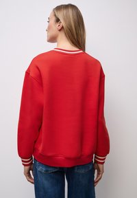 Rode sweatshirt met een ontspannen pasvorm, ronde nek en witte gestreepte accenten op de manchetten. Zacht materiaal met een gladde textuur.