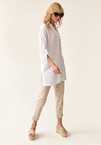 Hvid, letvægts, knap-opp tunika med lange ærmer og sideskår, parret med beige linnedbukser og vævede platform-sandaler.