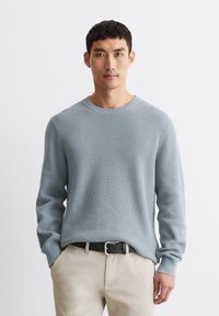 Helles blauer, gerippter Strickpullover mit langen Ärmeln und Rundhalsausschnitt, kombiniert mit beigen Hosen und einem schwarzen Gürtel.