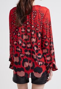 Top trasparente rosso con un motivo a stampa leopardata nero e rosso scuro. Design comodo con maniche a campana e orlo arrotondato.