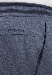 Tejido DRI-FIT azul con acabado texturizado, con un logo bordado y un detalle de bolsillo con cremallera, diseñado para la gestión de la humedad.