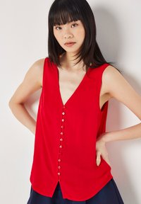 Red sleeveless top with a deep V-neck, button closure down the front, and a subtle textured pattern. Flared fit at the hem.
