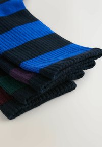 Multicolore sokken met ribbelstructuur. Kleuren zijn donkerblauw, zwart, groen en paars in horizontale strepen. Zacht gebreid materiaal.