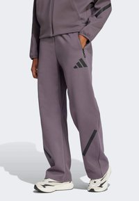 Pantalones deportivos morados con detalles y rayas negras, hechos de una tela suave, con bolsillos laterales y un ajuste relajado.