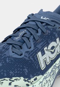 Scarpe da corsa blu con tomaia testurizzata, caratterizzate da un design a fantasia, lacci piatti e una suola leggera. Branding presente sul lato laterale.