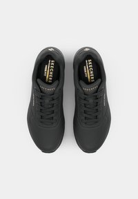 Paire de baskets Skechers larges noires avec lacets, vue de dessus sur fond clair uni.