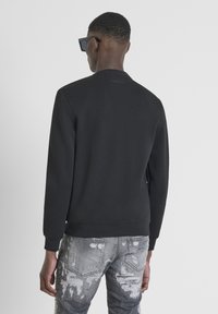 Sudadera negra con cuello redondo, puños acanalados y un diseño minimalista. Combinada con pantalones vaqueros grises desgastados que presentan un patrón desvanecido.