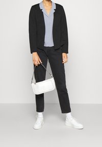 Černý blazer přes světle modrou košili s knoflíky, v kombinaci s černými džínami a bílými teniskami. Drží bílou kabelku s krokodýlími vzory.