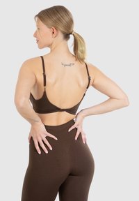 Brun, sømløs bralette med justerbare stropper, der har et snoet rygdesign. Matcher med højtaljede brune leggings. Glat tekstur.