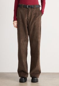 Brown corduroy pants with a wide-leg design, featuring vertical ribbed texture and a black belt. Paired with chunky black boots.