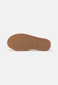 Semelle de chaussure en caoutchouc brun texturé, avec une surface lisse et une section de talon légèrement surélevée, avec un branding minimal.