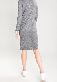 Graues, langärmliges Kleid aus strukturiertem Strickmaterial, knielang, mit lockerer Passform. Kombiniert mit weißen Turnschuhen.