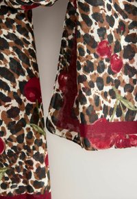 Šátek s leopardím potiskem, zdobený červenými třešněmi, hnědými tóny a průhlednou texturou. Okraje lemované burgundskou barvou, což vytváří jedinečný design.