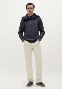 Marineblauwe longsleeve shirt met knoopsluiting, crèmekleurige rechte broek en donkere schoenen. Trui geknoopt om de nek voegt detail toe.