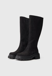 Μαύρες μπότες σουέντ μέχρι το γόνατο με χοντρή σόλα από καουτσούκ και πλαϊνό φερμουάρ. Ελαφρώς στρογγυλερή μύτη και άμεση σχεδίαση στο επάνω μέρος.