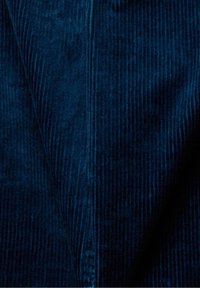 Tissu en velours côtelé bleu foncé avec des rainures verticales visibles et une texture douce, montrant des plis et des ombres dus au drapé.