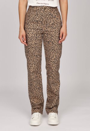 Pantalon léopard en tan et noir, fabriqué en tissu doux ; design à jambe droite avec taille haute, associé à des baskets blanches.