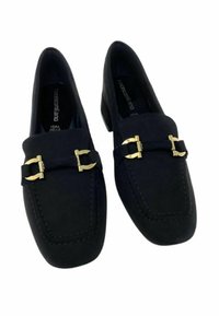 Mocassini in suede nero con accessorio distintivo in metallo dorato. Presentano una punta arrotondata e cuciture visibili lungo i bordi.