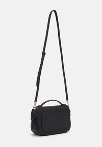 Musta nahkainen crossbody-laukku, jossa säädettävä hihna, yläkahva ja sivusolmion yksityiskohta, valkoista taustaa vasten.