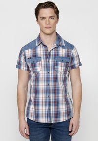 Camicia a maniche corte a quadri nei colori blu, rosso e bianco. Dettagli in denim sulle spalle e sulle tasche del petto; chiusura anteriore con bottoni.