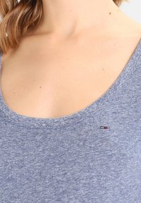 Light blue t-shirt with a wide scoop neckline, made of soft fabric, featuring a small logo in red, white, and blue on the front.