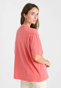 T-shirt corail surdimensionné, fabriqué en tissu doux, avec un col rond et des manches courtes. Design simple sans motifs ni accents visibles.