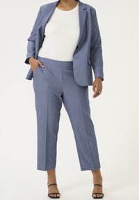 Vaaleansininen räätälöity bleiseri, jossa on yksi nappi, samansävyiset lyhyet housut ja valkoinen kireä t-paita. Teksturoitu kangas, jossa on hienovaraiset raidat.