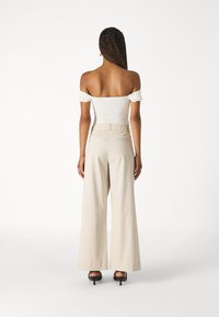 Biele off-the-shoulder tričko s volánikovými rukávmi skombinované so širokými béžovými nohavicami. Hladká textura, elastický pás a dĺžka do kolien.