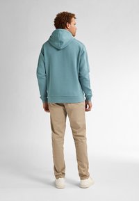 Lichtblauwe hooded sweatshirt met een ontspannen pasvorm, gecombineerd met beige broek en witte sneakers, die een eenvoudig, functioneel ontwerp tonen.