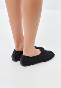 Černé boty na slip-on s měkkým textilním svrškem a hladkými koženými akcenty, které se vyznačují zaobleným designem špičky a flexibilní podrážkou.