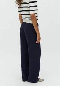 Navy wide-leg trousers with a smooth texture, featuring a tailored design and pockets. Paired with a black-and-white striped top.