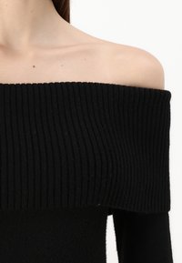 Sweater preto sem ombros com textura canelada larga no decote, tecido suave e mangas longas ajustadas.
