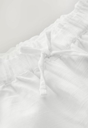 Vitt bomullstyg med en texturerad mönstring och snörning. Tyget har en mjuk, rynkad midjebanddetail.