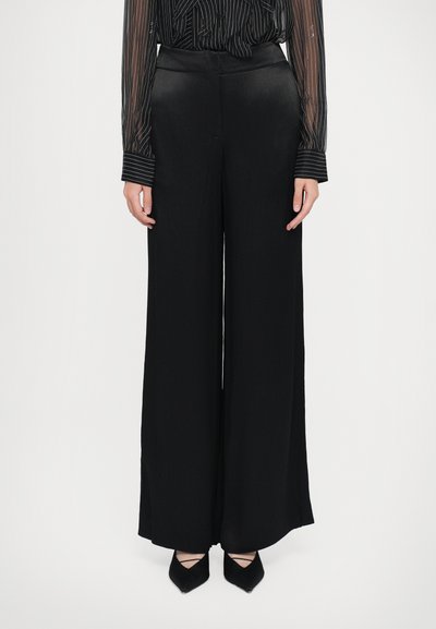 Pantalones anchos negros, hechos de una tela suave, con una cintura alta y un diseño limpio. Combinados con tacones negros de punta afinada.