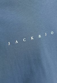 Sinine puuvillane t-särk, millel on sooneline tekstuur ja tekst "JACK & JO" valget värvi, paigutatud alumisse paremasse nurka.