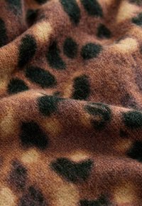 Tissu marron doux à texture pelucheuse présentant en gros plan des motifs irréguliers d'imprimé léopard noir et fauve.