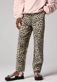 Pantalones de estampado de leopardo en tonos marrón y negro, de corte relajado, combinados con sandalias deslizantes metálicas plateadas con una sola gruesa negra.