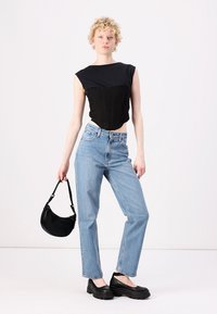 Top court noir avec corsage structuré, jeans droit bleu clair, et sac hobo noir. Chaussures à plateforme noires épaisses, design minimaliste.