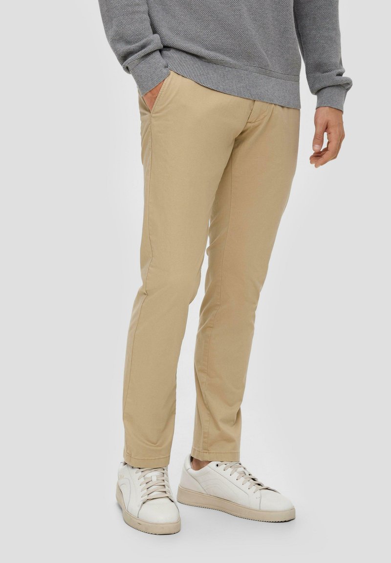Chinos beige à coupe ajustée, en toile de coton, dotés de poches latérales et associés à des baskets blanches pour un look décontracté.
