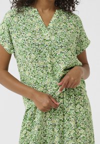 Bloemenjurk in groentinten, met een V-hals, korte mouwen en een geraffineerde taille. De stof heeft een gestructureerd, lichtgewicht uiterlijk.