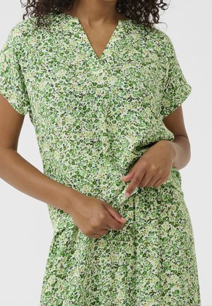 Floral dress in green tones, featuring a V-neck, short sleeves, and a gathered waist. The fabric has a textured, lightweight appearance.